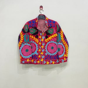 May include: A red embroidered jacket with colorful floral and leaf patterns. The jacket has a striped lining and a button closure.