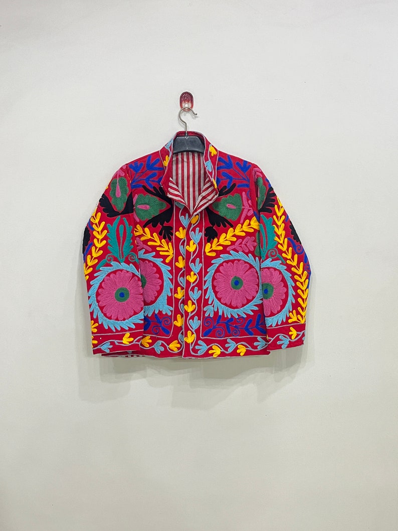May include: A red embroidered jacket with colorful floral and leaf patterns. The jacket has a striped lining and a button closure.