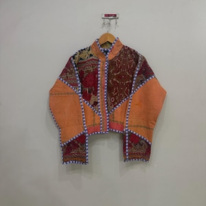 May include: A quilted jacket featuring a patchwork design with panels of orange, deep red, and dark brown fabric. The garment has a mandarin collar, long sleeves, and is accented with a light blue and white checkered trim along the edges and seams.