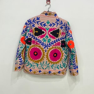 May include: A beige jacket with long sleeves and a high neck. The jacket is embroidered with colorful floral patterns in shades of pink, blue, green, orange, and black.