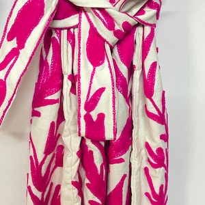 Puede incluir: Un vestido blanco con un patr&oacute;n de bordado floral rosa. El vestido tiene una faja que se ata a la cintura.