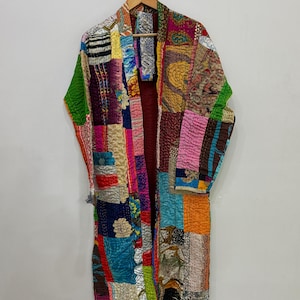 Peut inclure: Robe kimono patchwork aux couleurs vives, accrochée à un cintre en bois. Le vêtement est composé de différents morceaux de tissu aux couleurs variées : vert, rose, bleu et orange. Il présente une longue ouverture sur le devant.