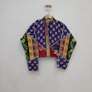 May include: A cropped jacket featuring a patchwork design with various floral and paisley patterns in shades of purple, red, yellow, and green. The garment has a high collar, long sleeves, and a front opening with a black and white striped trim.