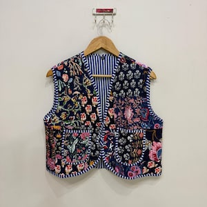 May include: A quilted vest with a patchwork design featuring floral patterns in shades of pink, yellow, and blue on a navy background. The vest has two pockets and a striped blue and white lining.