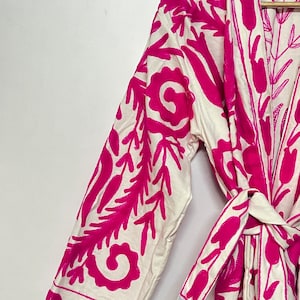 Puede incluir: Batista blanca con un dise&ntilde;o de bordado floral rosa. La bata tiene un cintur&oacute;n de lazo y mangas largas.
