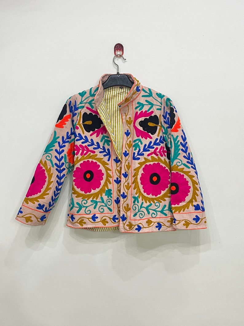 May include: A pink embroidered jacket with colorful floral patterns. The jacket has a mandarin collar and long sleeves.