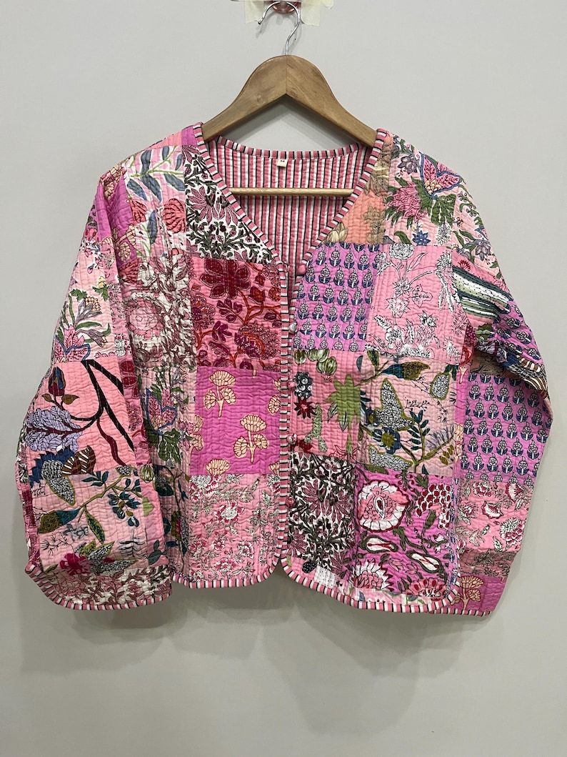 Op de afbeelding: Een roze gewatteerd jack met een patchwork-ontwerp met bloemenpatronen. Het jack heeft een V-hals en een knoopsluiting.