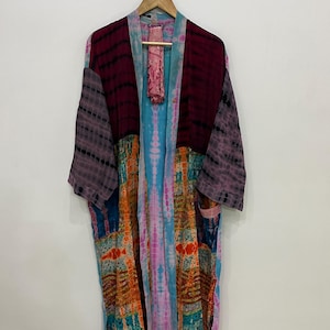 May include: A long, open-front kimono robe featuring a patchwork design with tie-dye patterns in shades of deep burgundy, light purple, bright orange, and turquoise blue. The garment has wide sleeves and a matching tie-dye fabric belt.