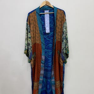 Op de afbeelding: Een lange kimono met open voorzijde en een patchworkontwerp van verschillende stoffen. Het kledingstuk toont een mix van blauwe, oranje en bruine tinten met ingewikkelde bloemen-, paisley- en geometrische patronen over de panden en mouwen.