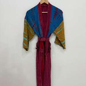 May include: A long-sleeved robe featuring a deep magenta base color with contrasting tie-dye patterns in shades of blue and mustard yellow on the sleeves and upper chest. The garment includes a matching fabric tie belt at the waist.
