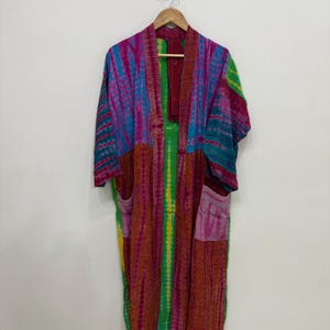 May include: A long-sleeved kimono-style robe featuring a vibrant tie-dye pattern in shades of magenta, teal, green, and yellow. The garment has an open front, a wide collar, and two large patch pockets on the lower front section.