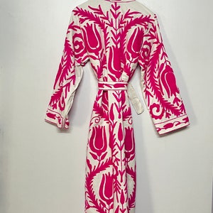 Puede incluir: Una bata blanca con un estampado floral rosa. La bata tiene mangas largas y un cintur&oacute;n de atar.