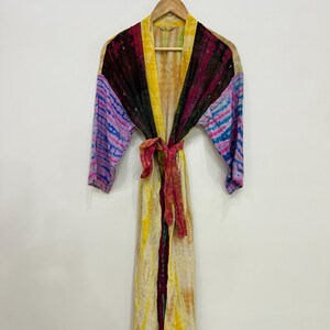 May include: A long-sleeved robe featuring a vibrant tie-dye pattern in shades of yellow, deep maroon, and purple. The garment includes a matching fabric tie belt at the waist, an open front design, and a light, flowing fabric construction.