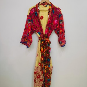 May include: A colorful, floral-patterned robe with a tie-waist. The robe features a vibrant mix of red, yellow, and blue hues, with intricate embroidered floral designs. The sleeves have a blue trim, and the robe is hanging on a wooden hanger.