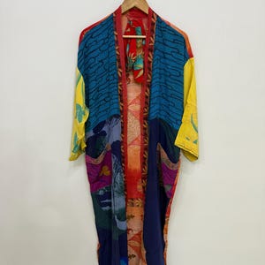 May include: A long, open-front kimono robe featuring a patchwork design with vibrant colors including blue, yellow, red, and orange. The garment displays various patterns such as abstract waves, floral motifs, and geometric shapes on a lightweight fabric.