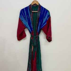 May include: A long-sleeved robe featuring a tie-dye pattern in shades of blue, teal, and deep red. The garment has an open front design with a matching fabric tie belt at the waist, hanging on a wooden hanger against a plain white wall.