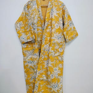 May include: A yellow quilted robe with a floral pattern. The robe has a long, open front and three-quarter sleeves.