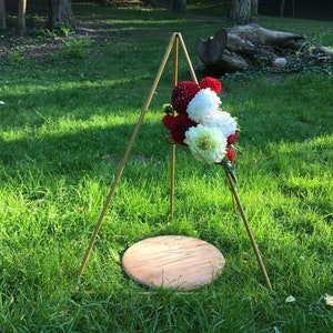May include: A gold metal tripod stand with a round wooden platform. A bouquet of red and white flowers is attached to the stand.