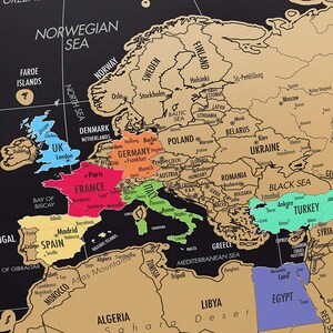 May include: A black and gold scratch-off world map with country outlines and city names. The map features colored regions for different countries, including the UK, France, and Italy. The text "NORWEGIAN SEA" is visible.