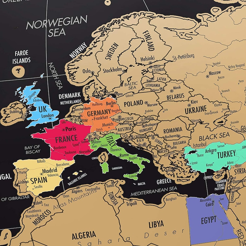 May include: A black and gold scratch-off world map with country outlines and city names. The map features colored regions for different countries, including the UK, France, and Italy. The text "NORWEGIAN SEA" is visible.