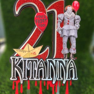 May include: Red and black glitter cake topper with the number 21, a paper boat with the text "SS Georgie", the text "You'll Float Too!" and the name "Kitanna". The topper features a character from the movie "It" holding a red balloon.