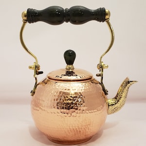 May include: A hammered copper teapot with a brass handle and spout. The teapot has a black wooden knob on the lid.