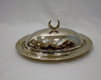 May include: A silver serving dish with a domed lid and a crescent moon finial. The dish has a hammered finish and a raised rim.