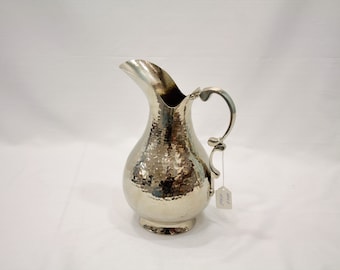 May include: A silver hammered metal pitcher with a curved spout and a decorative handle. The pitcher has a hammered texture and a round base.