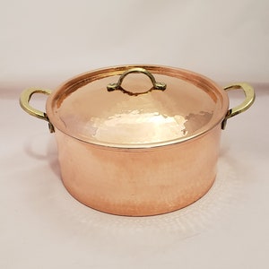 May include: A hammered copper pot with brass handles and a lid. The pot has a rounded body and a slightly flared rim.