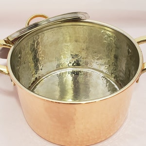 May include: A copper pot with a hammered finish and a brass handle. The pot has a silver-colored interior and a lid.