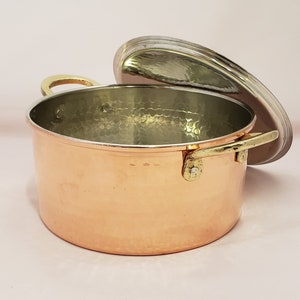 May include: A hammered copper pot with a brass handle and lid. The pot has a shiny, metallic finish and is suitable for cooking on the stovetop.