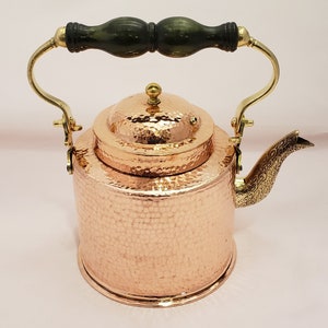 May include: A hammered copper teapot with a brass handle and spout. The teapot has a wooden knob on the lid.