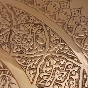 May include: Close-up of a copper tray with intricate embossed floral patterns. The tray has a warm, metallic sheen and a slightly rounded shape.