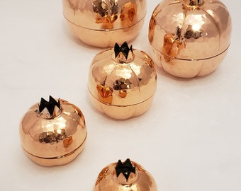 May include: Set of five copper pomegranate shaped boxes with hammered texture. The boxes are different sizes and are arranged in a row from largest to smallest.