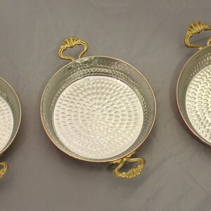 Op de afbeelding: Drie koperen serveerschalen met gehammerde oppervlakken en goudkleurige handvatten. De schalen zijn gerangschikt van klein naar groot.