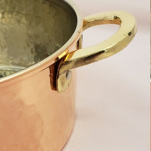 May include: A copper pot with a hammered finish and a brass handle. The pot is round and has a wide opening.