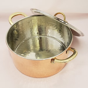 May include: A hammered copper pot with a silver lid and brass handles. The pot is empty and the lid is slightly ajar.