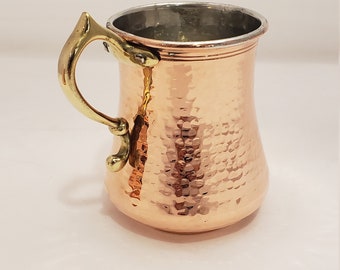 May include: A hammered copper mug with a brass handle. The mug has a rounded body and a slightly flared lip.