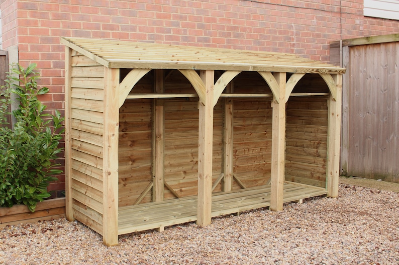 May include: A wooden log storage shed with a slanted roof and three open compartments. The shed is made of natural wood and has a rustic appearance.