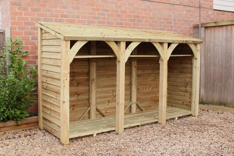 May include: A wooden log storage shed with a slanted roof and three open compartments. The shed is made of natural wood and has a rustic appearance.