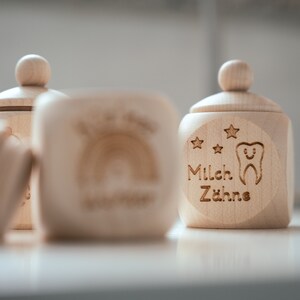 May include: Two wooden boxes with lids, one with a rainbow design and the other with the text "Milch Z&auml;hne" and a tooth with a smiley face.
