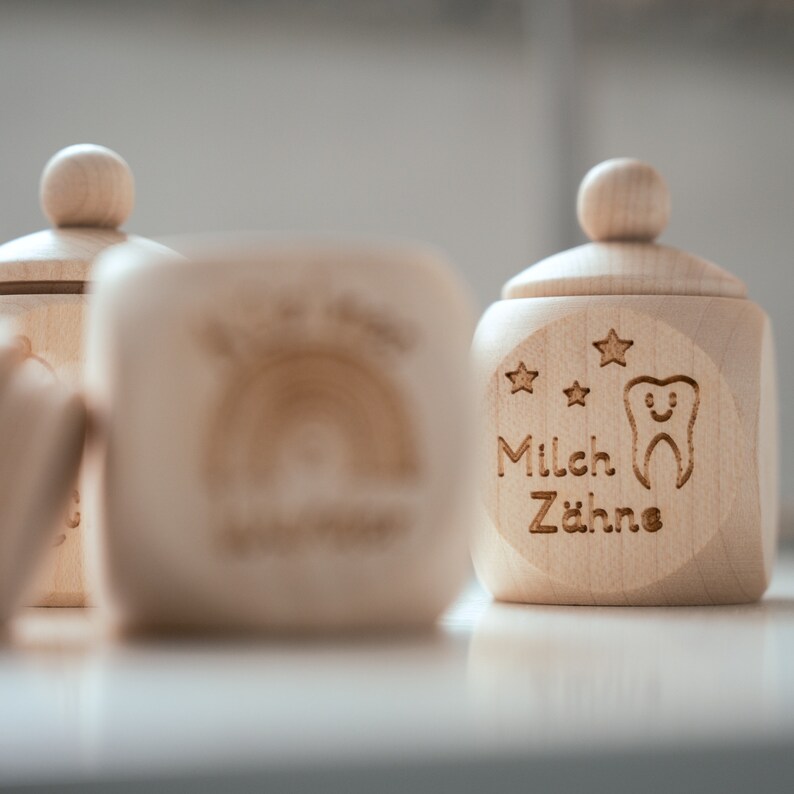 May include: Two wooden boxes with lids, one with a rainbow design and the other with the text "Milch Z&auml;hne" and a tooth with a smiley face.