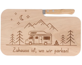 Könnte beinhalten: Helles Holzschneidebrett mit integriertem Griff. Das Brett zeigt ein eingraviertes Design eines Wohnmobils, Berge, Bäume, Sterne und den Text "Zuhause ist, wo wir parken!"