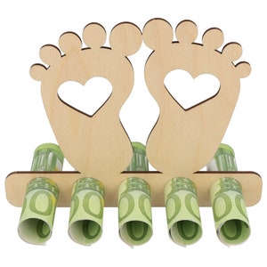 May include: A wooden money holder shaped like two feet with heart cutouts. The holder has slots for rolled-up currency, with several rolls of green and white bills visible. The design is light brown.