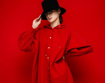 May include: A long, bright red hooded coat with gold buttons and a black top hat. The coat has long sleeves and a drawstring hood. The background is a solid red.