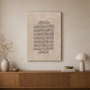 May include: A rectangular wall art piece featuring intricate black Arabic calligraphy printed on a textured, light beige canvas. The script is arranged in a vertical block format, centered on the canvas, showcasing traditional lettering styles.