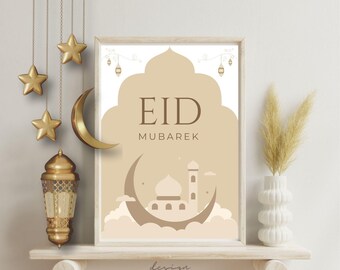 Puede incluir: Una impresión enmarcada con las palabras "EID MUBAREK" en letras marrones, con la silueta de una mezquita dentro de una luna creciente. Estrellas doradas decorativas, una luna creciente y una linterna cuelgan de arriba. Un jarrón blanco con plantas secas a la derecha.