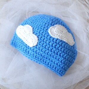 May include: A blue crocheted hat with two white crocheted clouds on top.