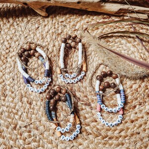 May include: Four beaded bracelets with different team names and colors. The bracelets are made with brown wooden beads, white beads, and black and white striped beads. The team names are "Wildcats", "Shockers", "Jayhawks", and "Tigers".