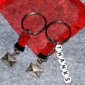 May include: Two red and silver keyrings with a red post box charm and a silver envelope charm. One keyring has a charm with the word "THANKS" spelled out in white letters.